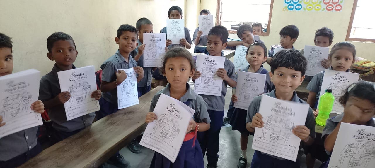 Assam students holding Phonics Pupil Book 1 in class